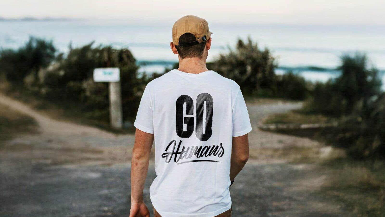 Person im weißen T-Shirt mit Lettering „Go Humans“ am Strand