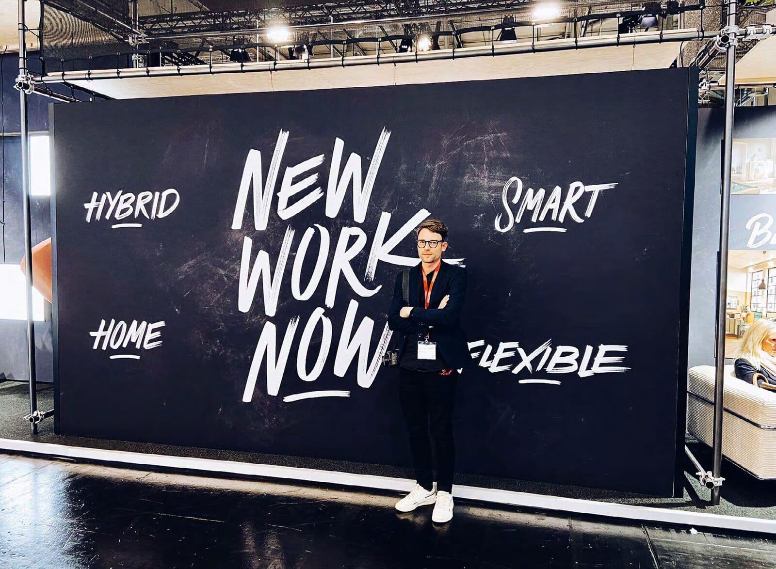 Handgeschriebenes Lettering „New Work Now“ auf einer großen schwarzen Messewand
