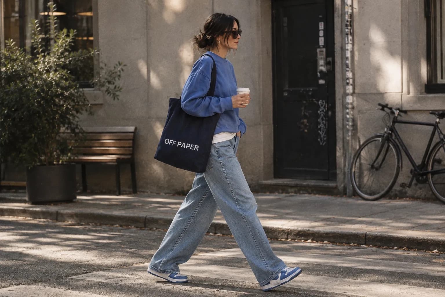 Person in weiter Jeans auf der Straße, mit Kaffeebecher und Tasche „OFF PAPER“