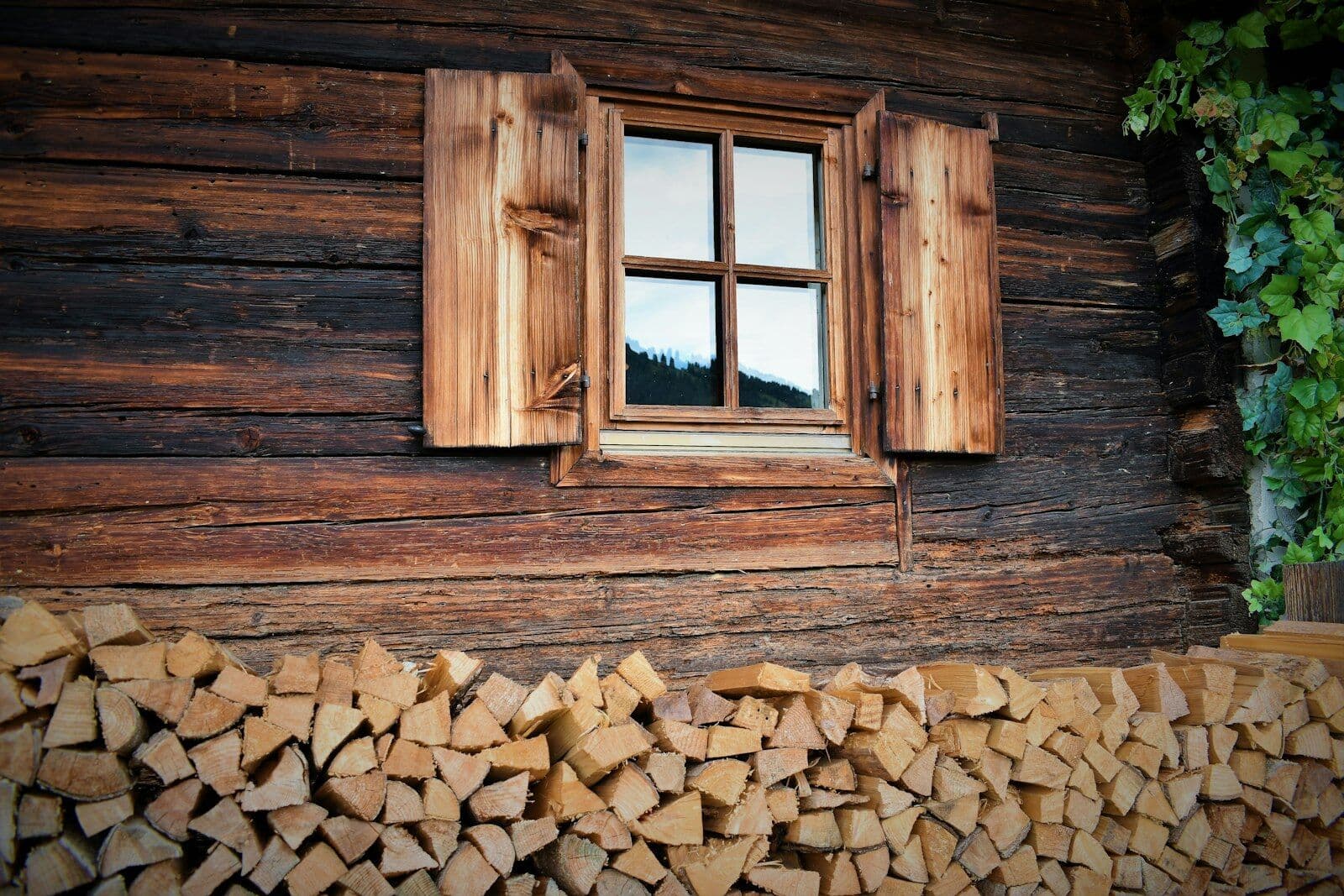 Holzfassade mit Fenster, Fensterläden und gestapeltem Brennholz