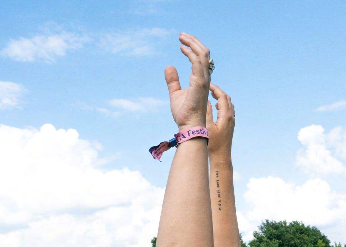 Erhobene Hand mit Festivalbändchen vor blauem Himmel